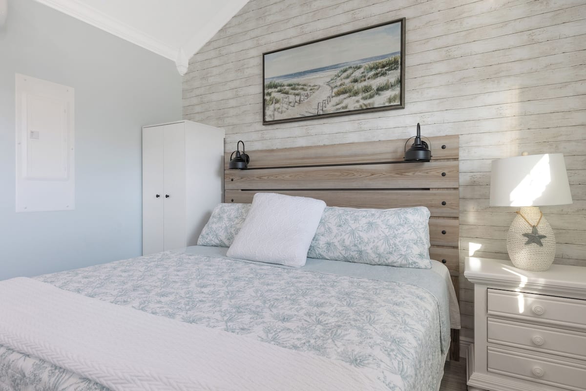A bedroom with a bed, a nightstand, a lamp, a framed picture on the wall, and a wardrobe.