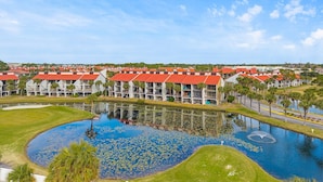 Un complexe hôtelier composé de plusieurs bâtiments aux toits rouges et dotés de balcons, avec un bassin central orné de nénuphars et un terrain de golf en premier plan.