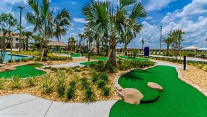 Un campo de golf con piscina, palmeras y un cielo azul despejado.