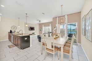 Una cocina moderna con una isla central, un comedor con sillas blancas y vistas al exterior.