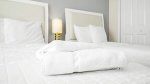 Una cama bien hecha con sábanas y almohadas blancas, una lámpara de noche y una puerta blanca en una habitación de hotel.