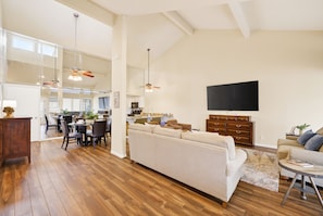 A spacious living area with a large sofa, dining table, and kitchen in the background. - Quaint, Cozy, Lakefront Haven w/ Lily Pad, Kayaks, Firepit, and Wrap Around Deck (Montgomery)