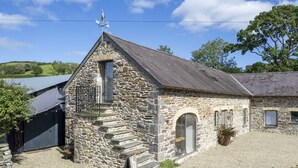 A stone building with a sloped roof, a small balcony, and a door with a window. - Cartws at Pentrecelyn- A Stylish Countryside Haven (Carmarthen)