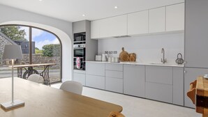A modern kitchen with grey cabinets, a wooden table, and a view of the outside. - Cartws at Pentrecelyn- A Stylish Countryside Haven (Carmarthen)