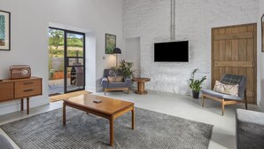 A modern living room with a stone wall, a flat-screen TV, a wooden coffee table, a sofa, and a chair. - Cartws at Pentrecelyn- A Stylish Countryside Haven (Carmarthen)