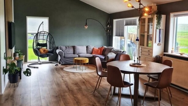 Un salon moderne comprenant un canapé, un fauteuil suspendu, une table à manger avec des chaises et une grande fenêtre donnant sur l’extérieur.