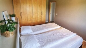 Une chambre avec une grande armoire en bois, un lit recouvert de draps blancs et une petite plante en pot.