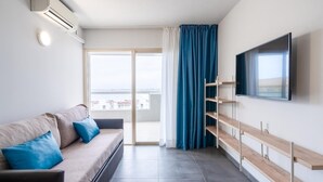 A modern living room with a sofa, a mounted TV, and a sliding glass door leading to a balcony. - APCOSTAS Blue Beach two bedrooms (Salou)