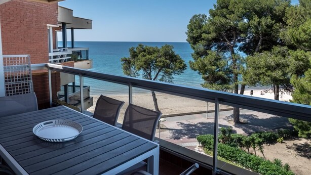 Un balcón con mesa y sillas, con vista a una playa y al mar.