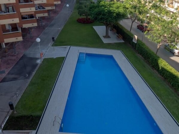 En rektangulær swimmingpool med en klar, blå vandoverflade, omgivet af en velplejet græsplæne og nogle få træer.