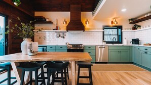 Une cuisine moderne avec des poutres en bois, des meubles de couleur verte et un îlot central doté de tabourets.