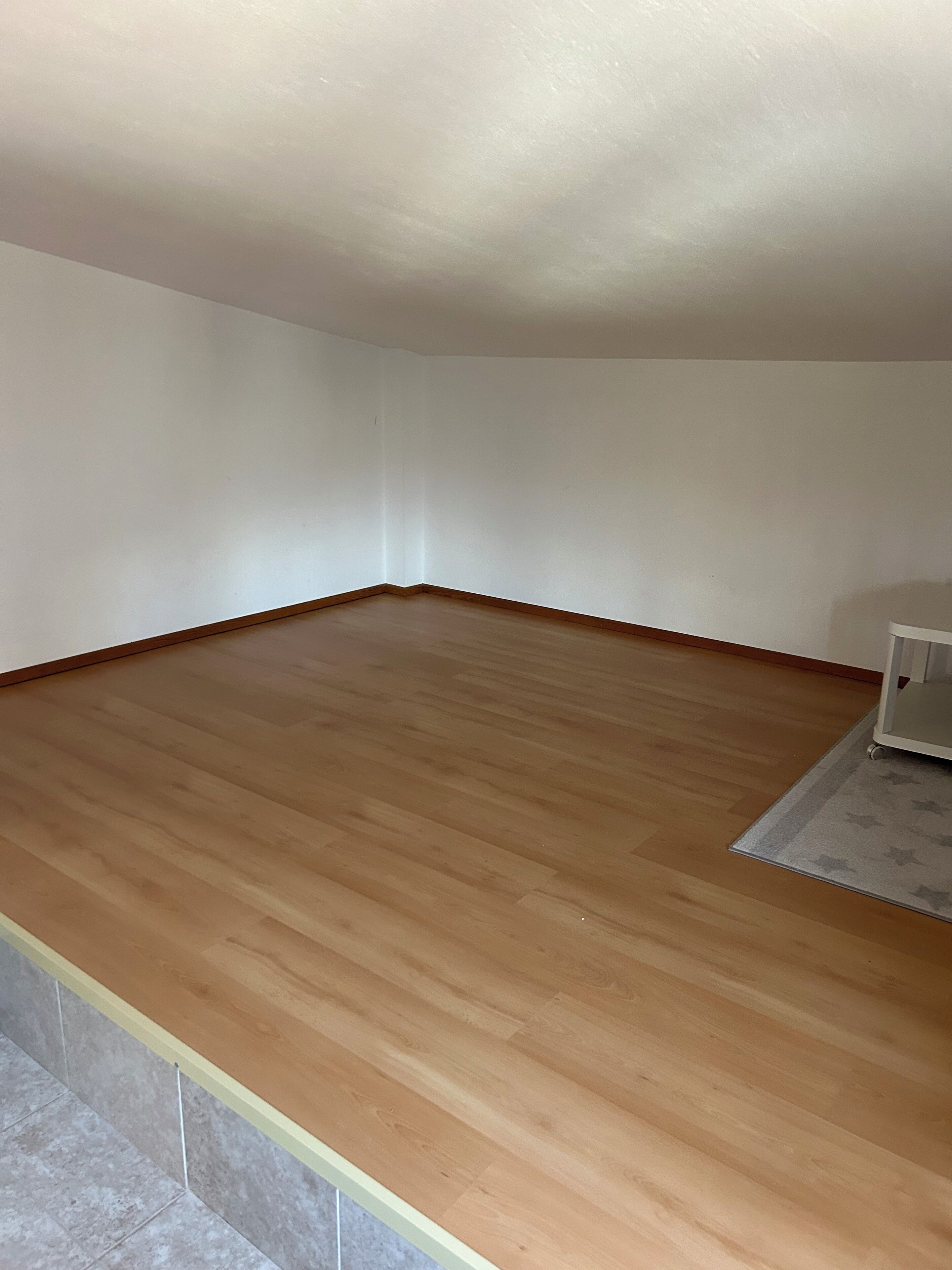 A room with a wooden floor, white walls, and a small white cabinet.