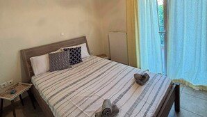 Una camera da letto con soffitto in legno, un letto con lenzuola a righe, un comodino e una finestra con tende.
