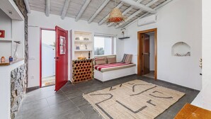 A modern interior with a stone wall, a red door, a bench with cushions, and a hanging light fixture. - Casa do Jardim Secreto - Monsaraz (Corval)