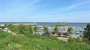 A marina with boats docked, a lighthouse in the distance, and a residential area with houses.