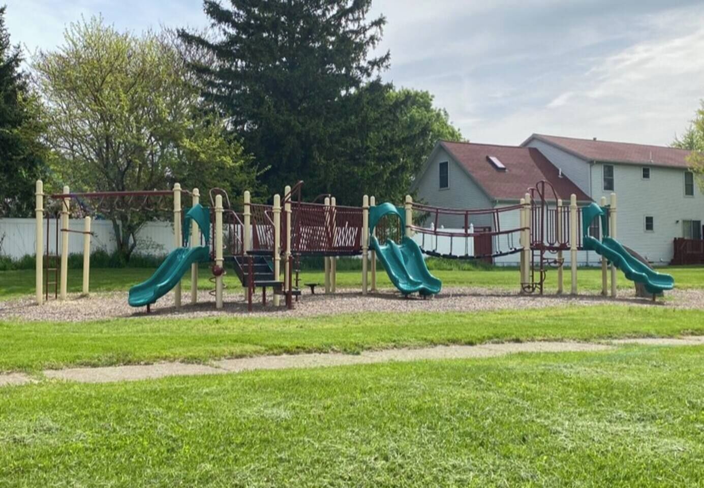 A playground with slides and climbing structures, surrounded by a grassy area and a building in the background.