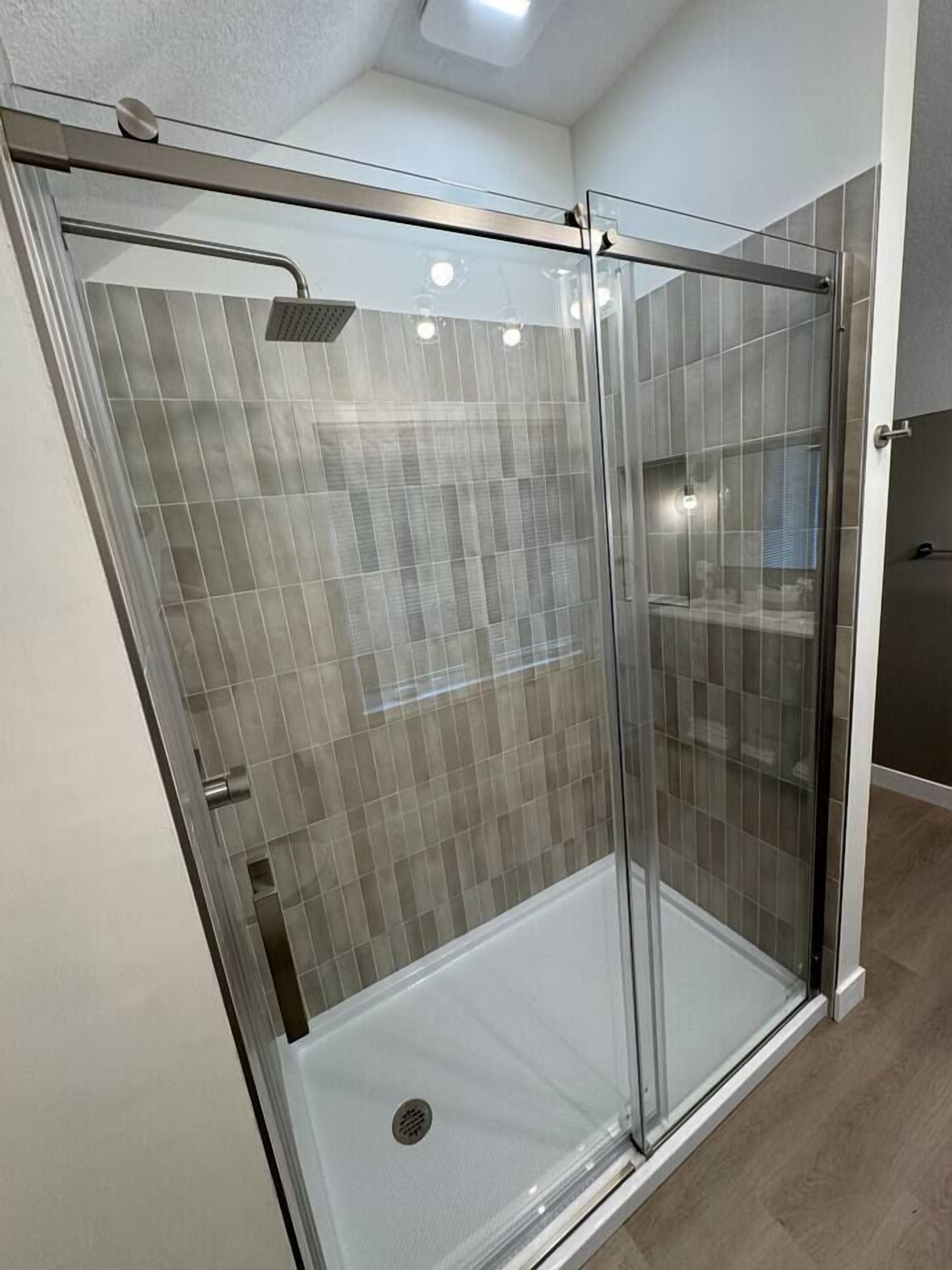 Ducha amb envàs de vidre, paret de rajola i terra blanca.