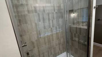 Ducha amb envàs de vidre, paret de rajola i terra blanca.