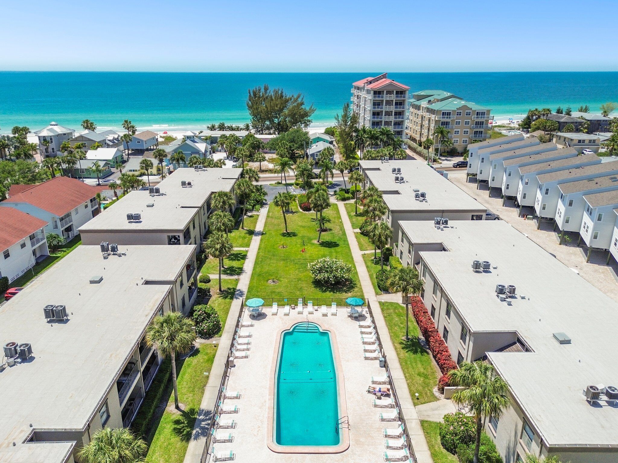 A resort with a central swimming pool, multiple buildings, and a beach view.