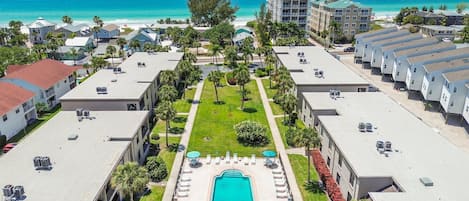 A resort with a central swimming pool, multiple buildings, and a beach view.