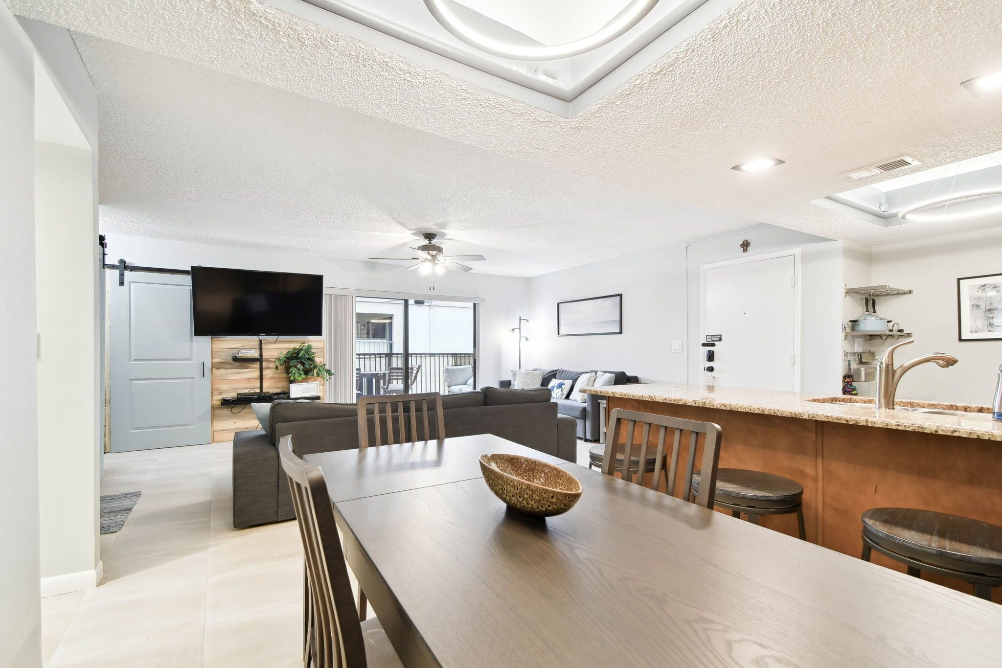 A modern kitchen with a dining area, a ceiling fan, and a large window.