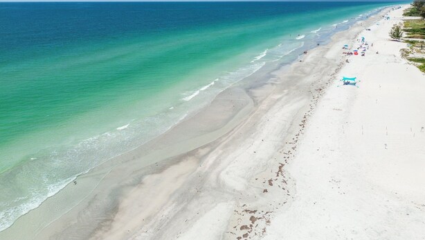 Ein Strand mit klarem türkisblauem Wasser, einem Sandstrand und einigen Sonnenschirmen.