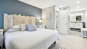 Ein Schlafzimmer mit einem großen Bett, einem Nachttisch, einem Deckenventilator und einem durch eine offene Tür einsehbaren Badezimmer.