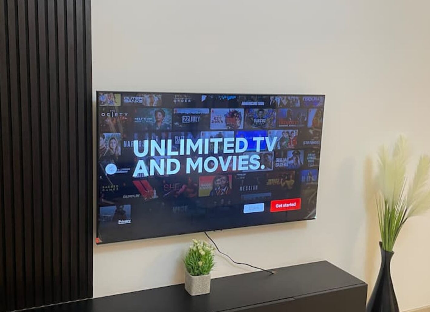Televisor de pantalla plana montado en la pared mostrando una interfaz de servicio de transmisión con el texto 'TELE Y PELÍCULAS ILIMITADAS'.