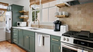 Una cocina moderna con gabinetes verdes, encimera blanca, estufa, microondas y cafetera.