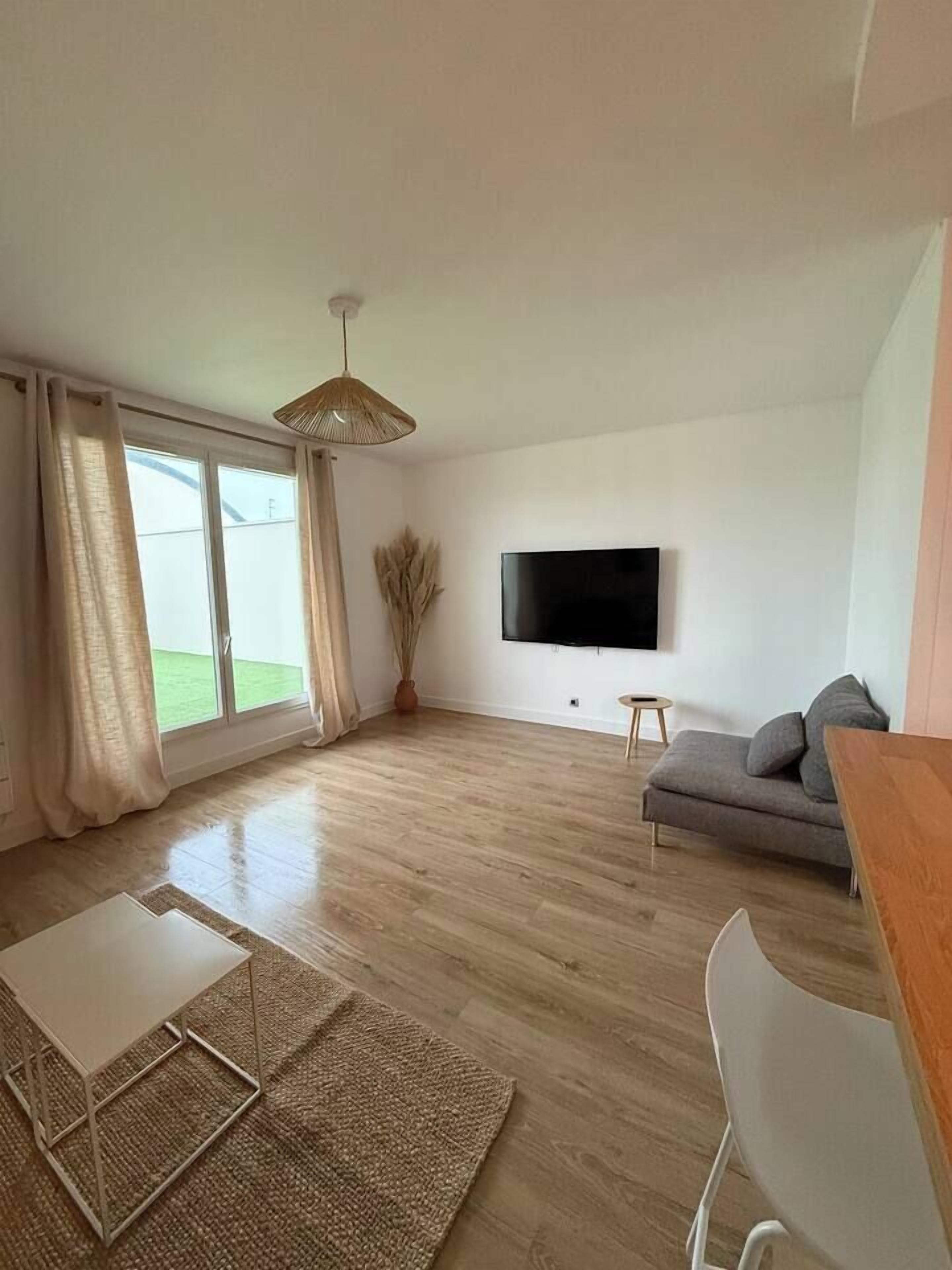Een moderne woonkamer met een grote televisie, een bank, een eettafel en uitzicht op de omgeving via een schuifdeur.