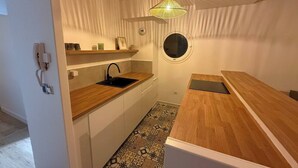 A compact kitchen with a round window, a hanging light fixture, and a patterned floor.