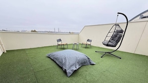 A rooftop terrace with artificial grass, a hanging chair, two chairs, and a table.