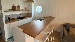 A compact kitchen with a wooden countertop, a sink, and a window. There is a white chair and a sofa in the adjacent living area.