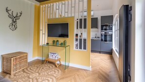 Un salon moderne avec une table basse en verre, un téléviseur à écran plat et un élément décoratif mural.