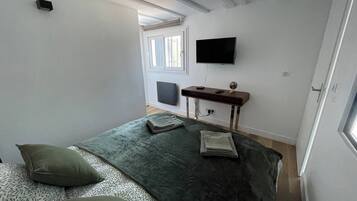A bedroom with a bed, pillows, a desk, a chair, a flat-screen TV, and a window.