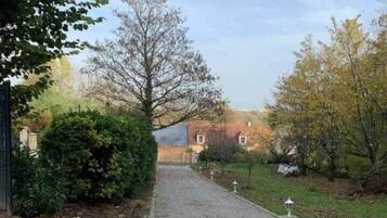 A gravel driveway leading to a building with a red roof, surrounded by trees and shrubs.