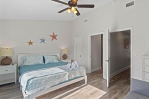 A bedroom with a bed, nightstands, a ceiling fan, and star decorations on the wall.