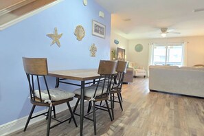 A dining area with a table and chairs, a sofa, and a ceiling fan in a room with wooden flooring and blue walls. - Townhome · Walk to Beach · Screened Porch · Pools (Port St. Joe)