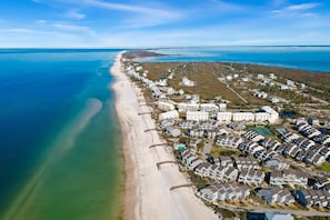 Vista aérea de una zona residencial costera con propiedades frente a la playa, un gran complejo hotelero y una vista despejada del océano.