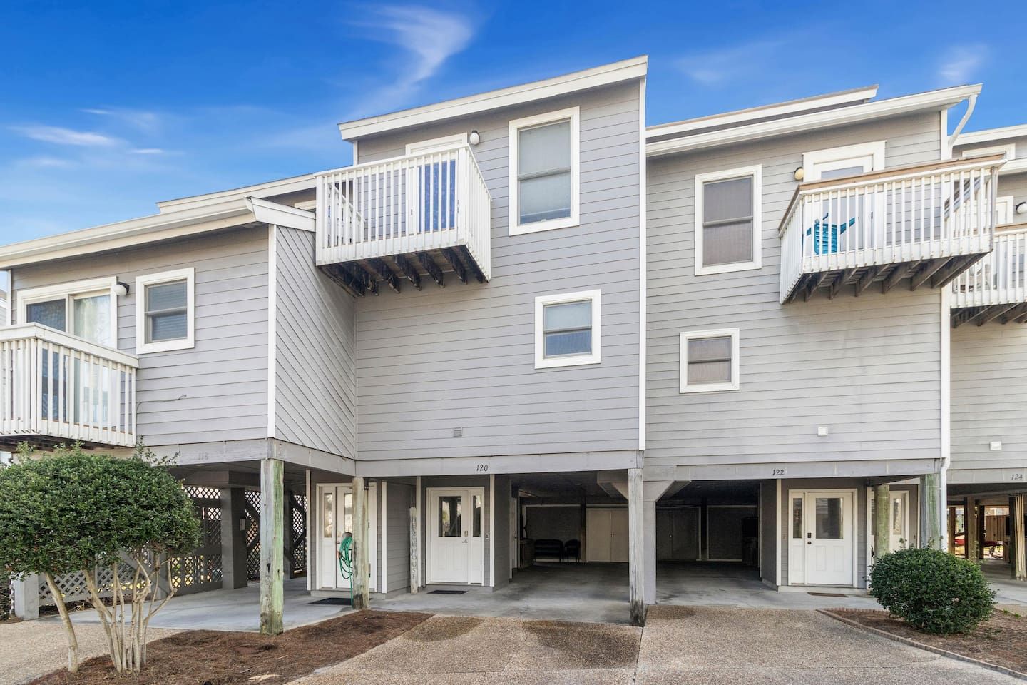 A multi-story residential building with balconies, a covered entrance, and a landscaped front yard.