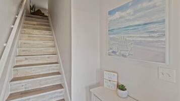 A staircase with wooden steps, a wall-mounted painting of beach chairs, and a sign that reads 'CATCH ME BY THE SEA.'