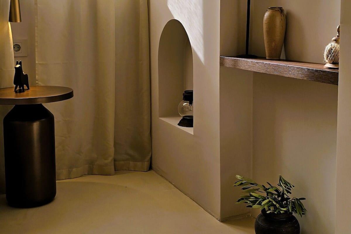 Una stanza dal design minimalista, con un tavolo rotondo, una lampada, una pianta in vaso e uno scaffale con oggetti decorativi.