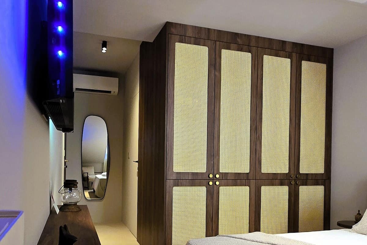 Una camera d'albergo con un letto, un armadio in legno, uno specchio e una TV a muro con luci blu.