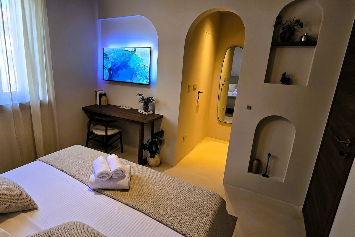 Una camera d'albergo con un letto, una scrivania, una televisione e un bagno con uno specchio.