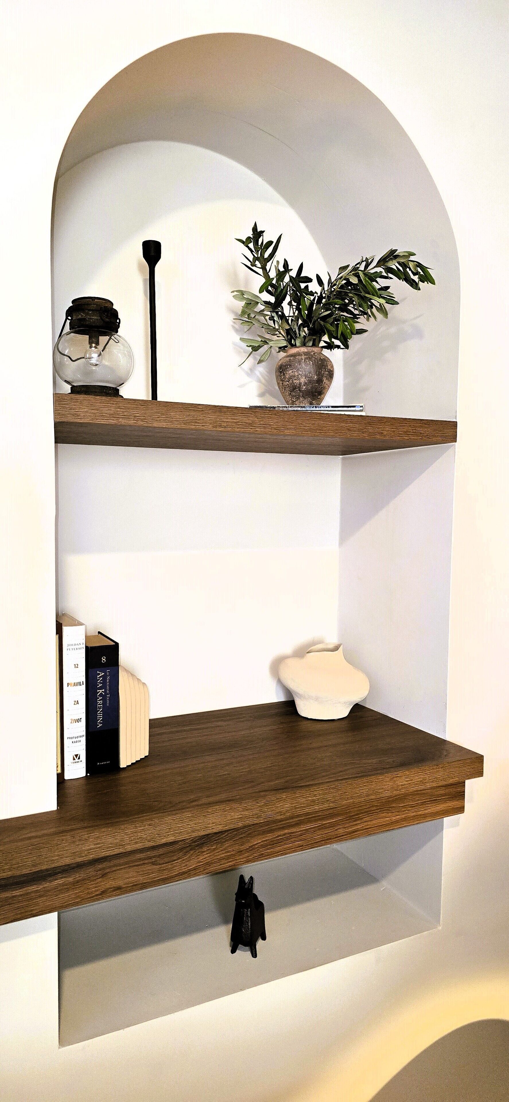 A wall-mounted wooden shelf with a potted plant, a lantern, and books.