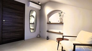 A modern bedroom with a dark wooden door, a large mirror, a white chair, and built-in shelves with decorative items. - Casa Beast (Split)