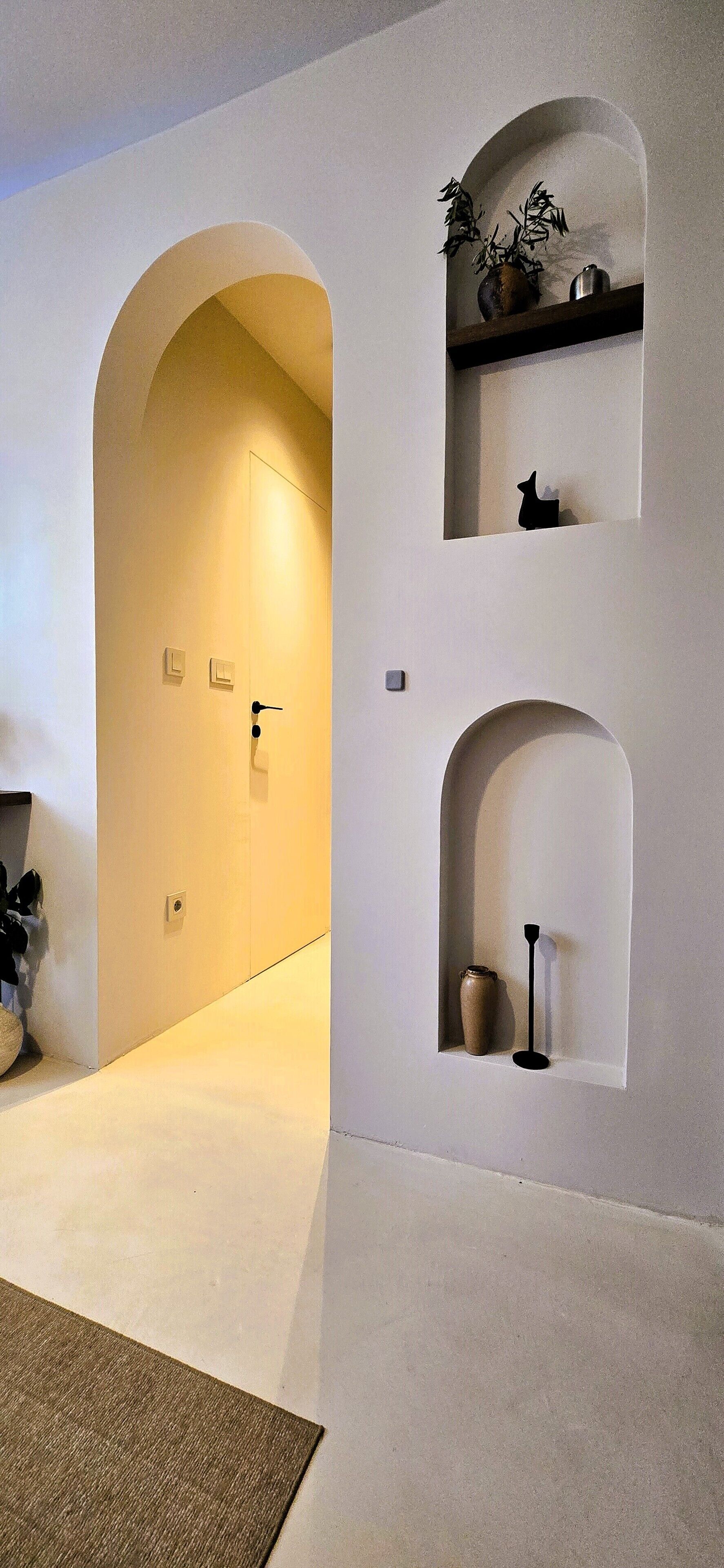 A hallway with a door, a small shelf with a plant, and a vase.
