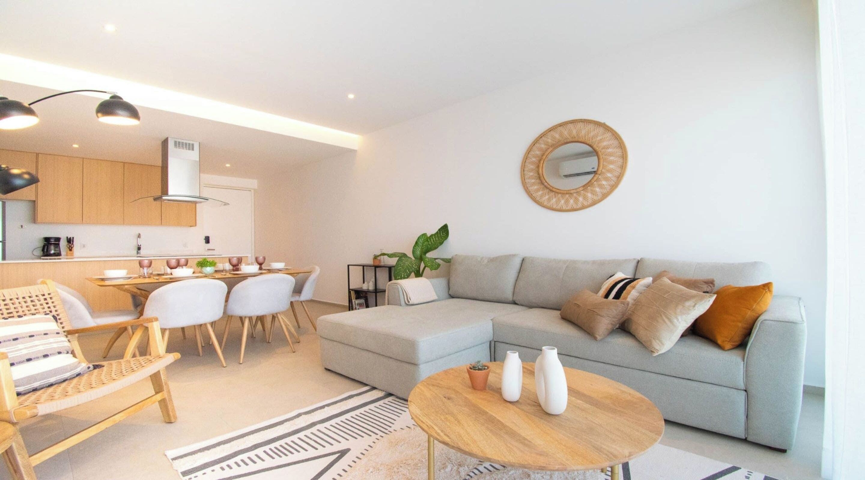 Un salon moderne avec un canapé gris, une table basse ronde et un coin repas comprenant une table et des chaises en bois.