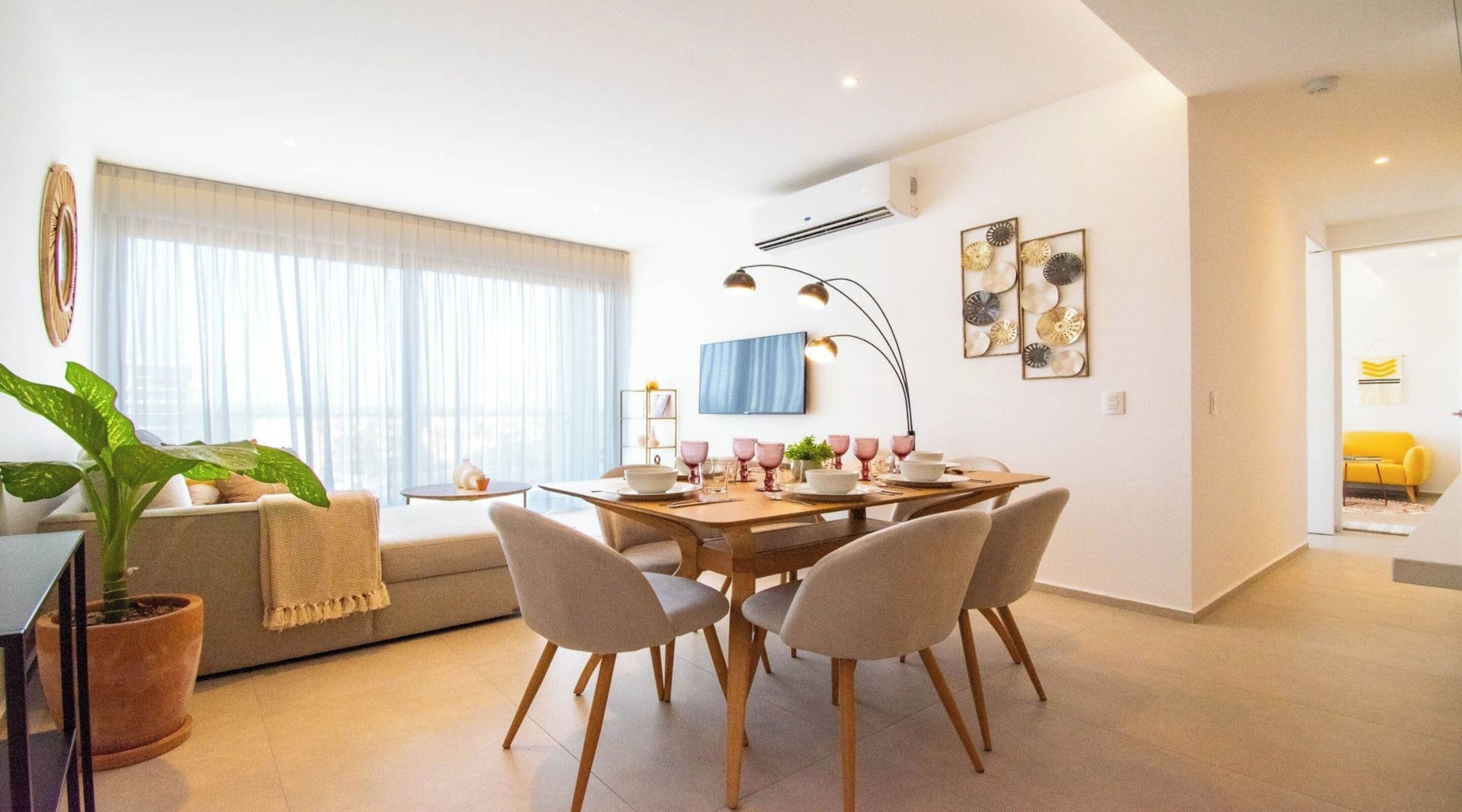 A modern living room with a dining area, featuring a sofa, a coffee table, a potted plant, and a dining table set for four.