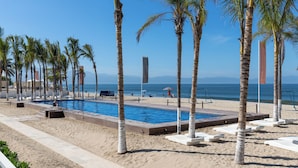 A poolside area with a clear view of the ocean, surrounded by palm trees and a sandy beach. - Condo Aria Ocean 614 by Kivoya (Nuevo Nayarit)